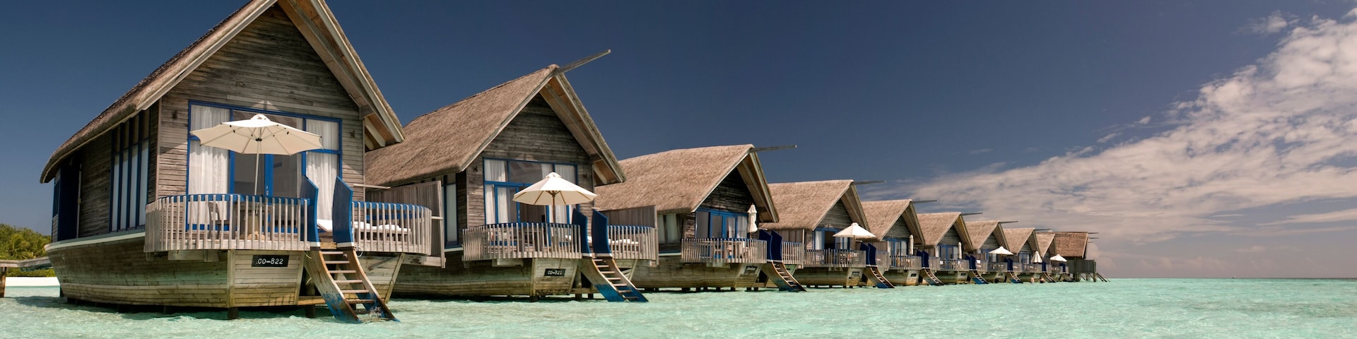 Cabañas sobre el agua con techos de paja y barandillas de madera, en un mar turquesa cristalino.