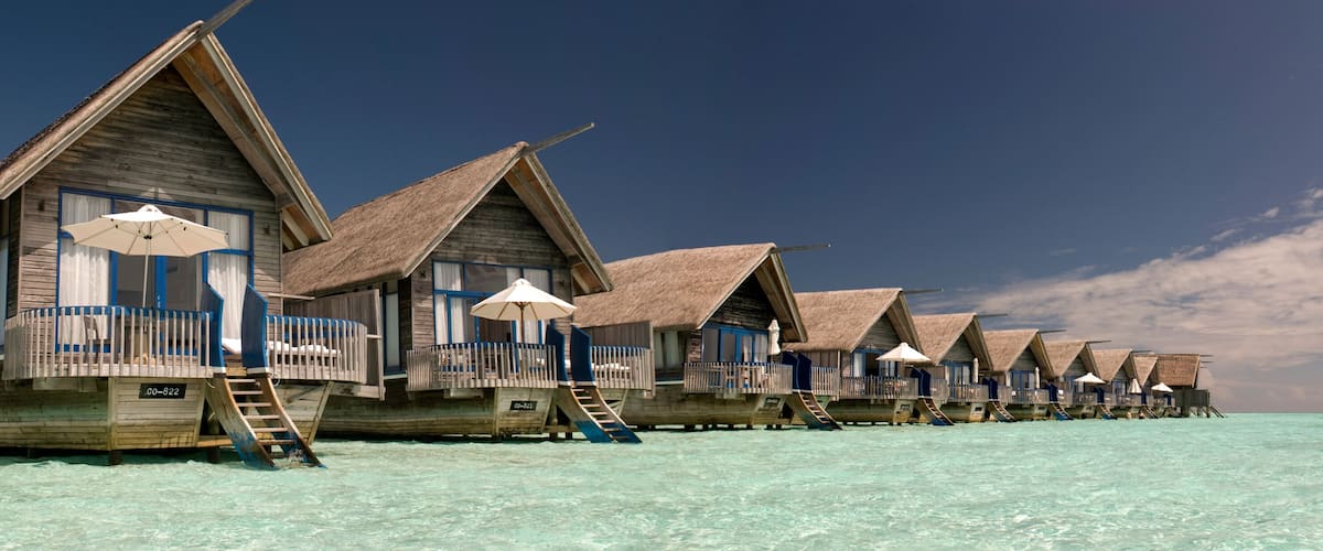 Overwater bungalows with thatched roofs and wooden railings on a clear turquoise sea.