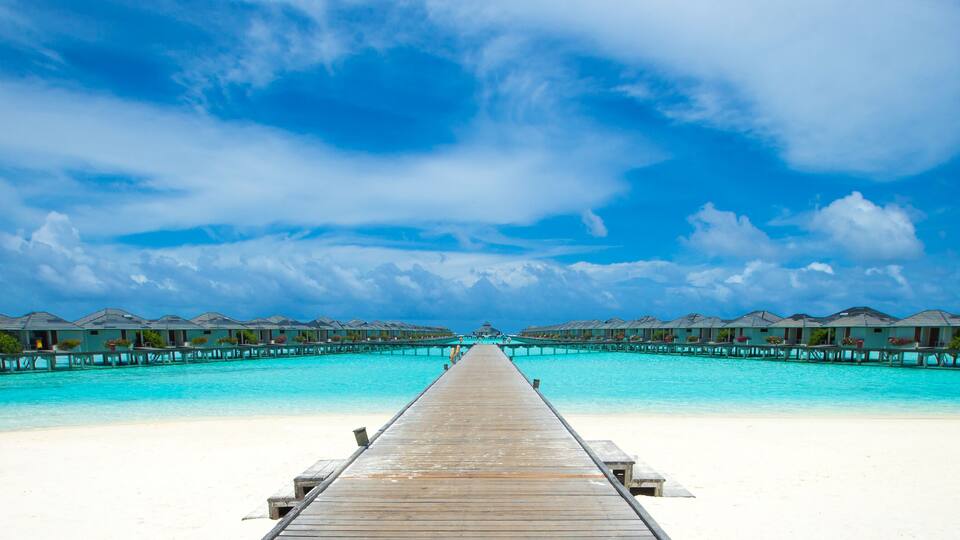 A wooden pier leading to overwater bungalows on a turquoise beach.