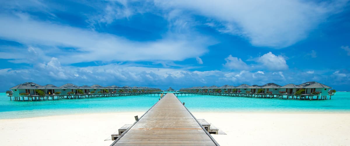 A wooden pier leading to overwater bungalows on a turquoise beach.