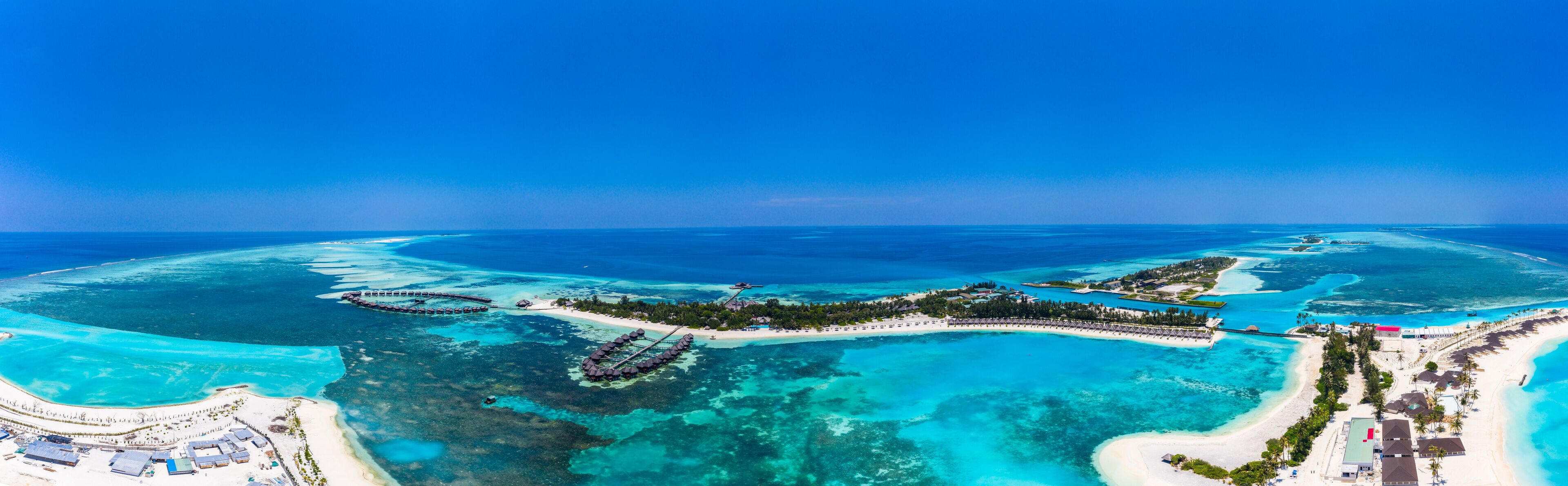 An aerial view of a tropical island with clear turquoise waters, overwater bungalows, and a white sandy beach.