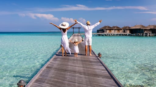 A happy family in white summer clothing on vacation walks along a wooden pier over tropical, turquoise ocean in the Maldives, Indian Ocean