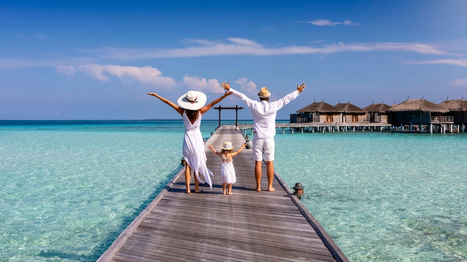 A wooden pier extending into turquoise water with overwater bungalows in the background.