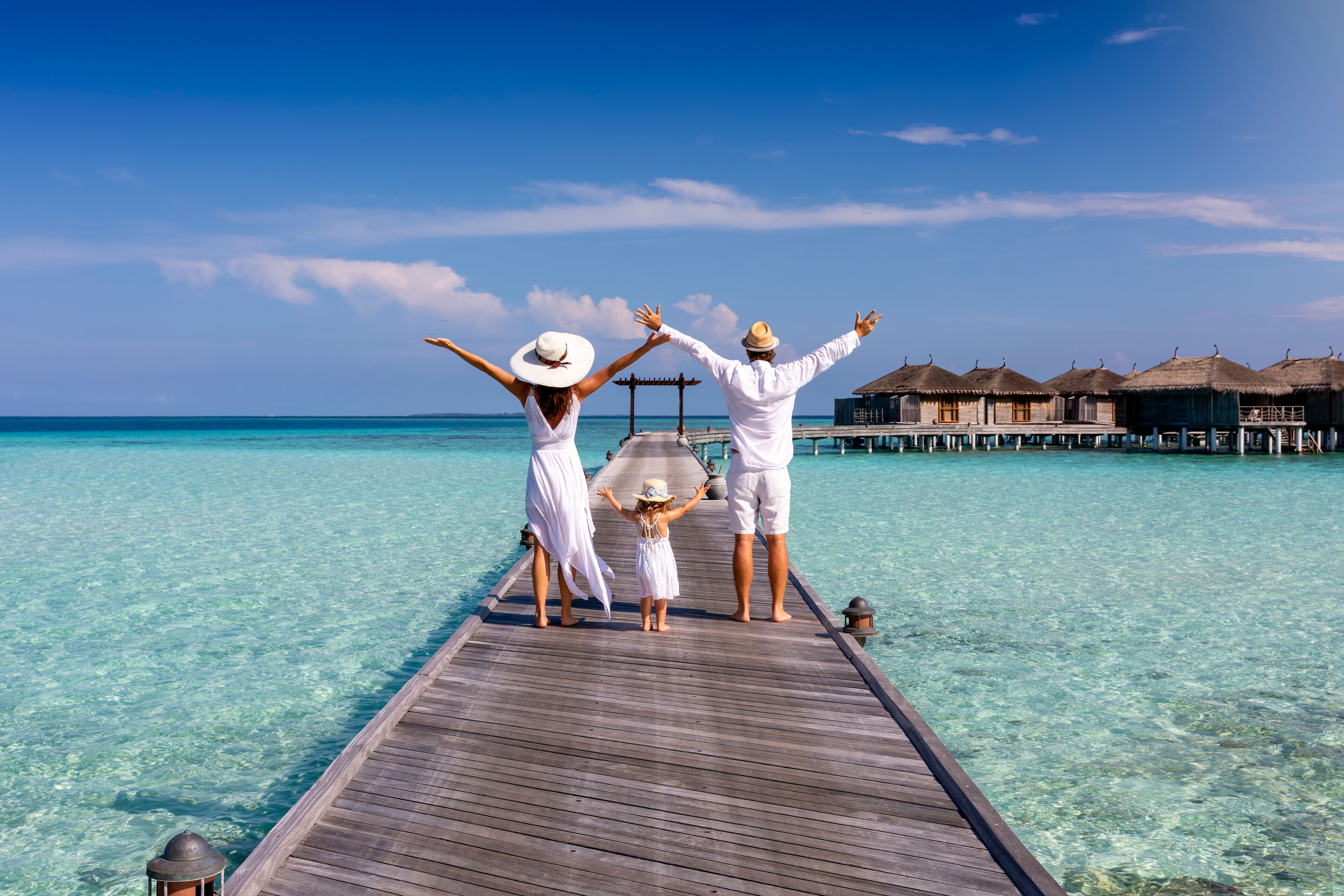 A wooden pier extending into turquoise water with overwater bungalows in the background.