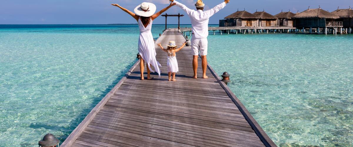 A wooden pier extending into turquoise water with overwater bungalows in the background.
