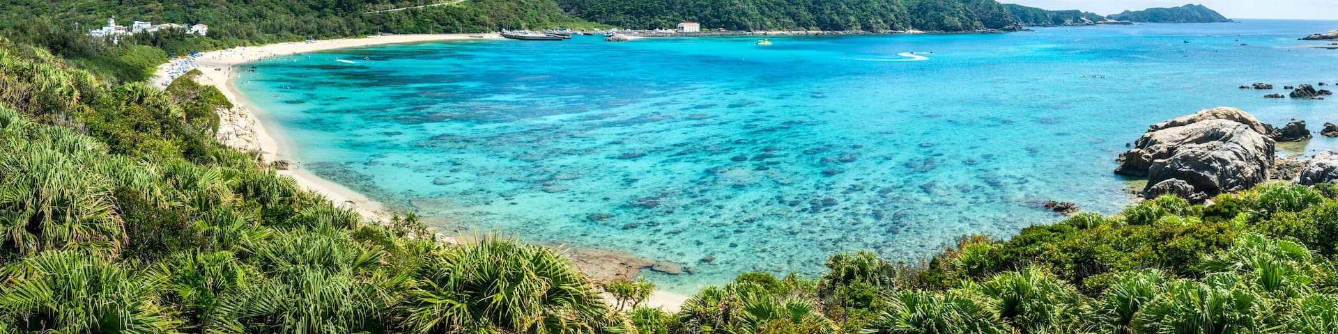 A tropical beach with clear turquoise waters, a sandy shore, and lush green hills in the background.