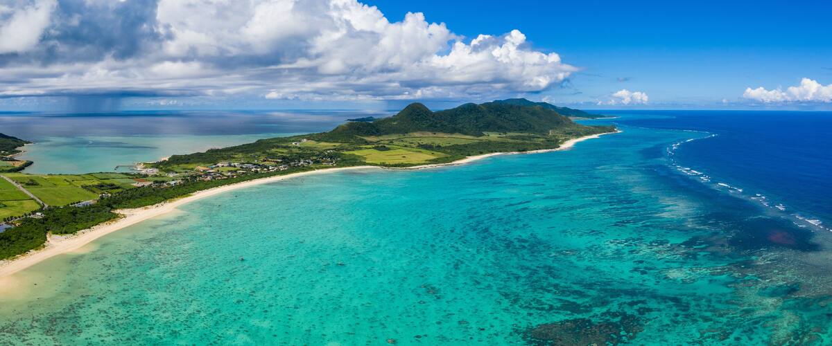 A coastal landscape with a clear turquoise sea, a sandy beach, and a mountainous island.