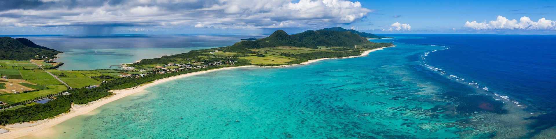 A coastal landscape with a clear turquoise sea, a sandy beach, and a mountainous island.
