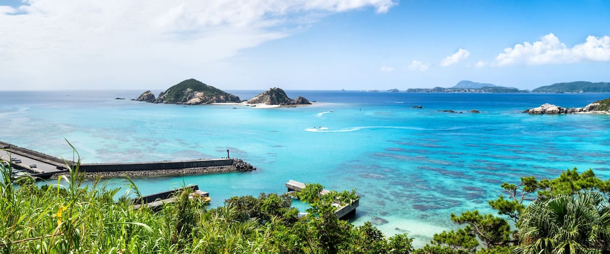 A tropical beach with clear turquoise waters, a pier, and lush greenery.