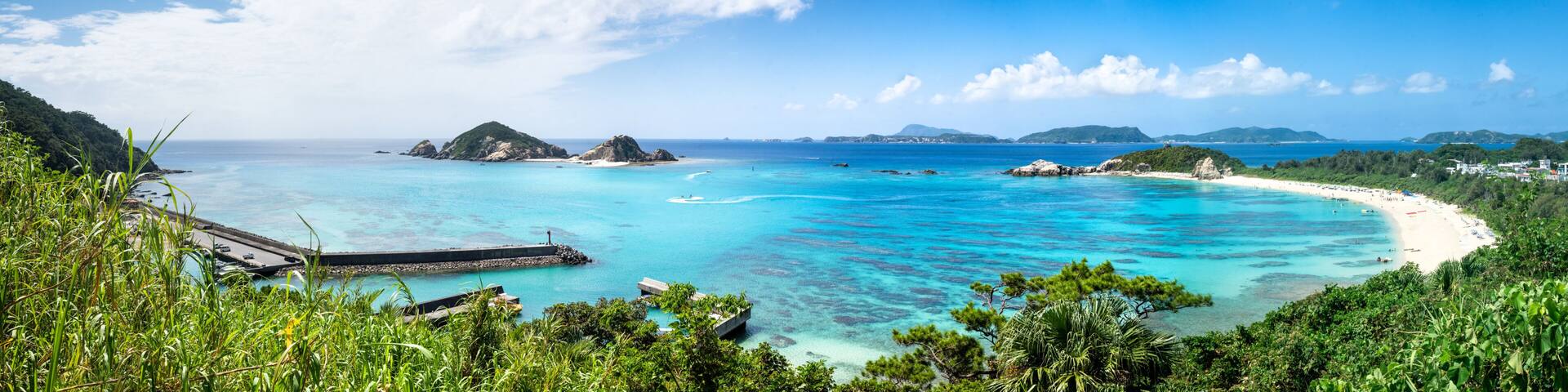 A tropical beach with clear turquoise waters, a pier, and lush greenery.