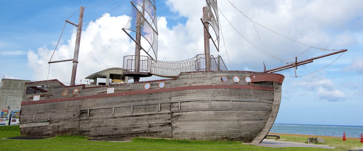 A large wooden ship with multiple masts and a cabin structure, situated on a grassy area near a body of water.