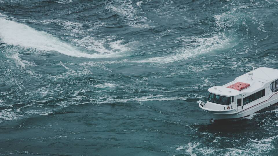 A white boat with a red deck navigating through choppy waters.