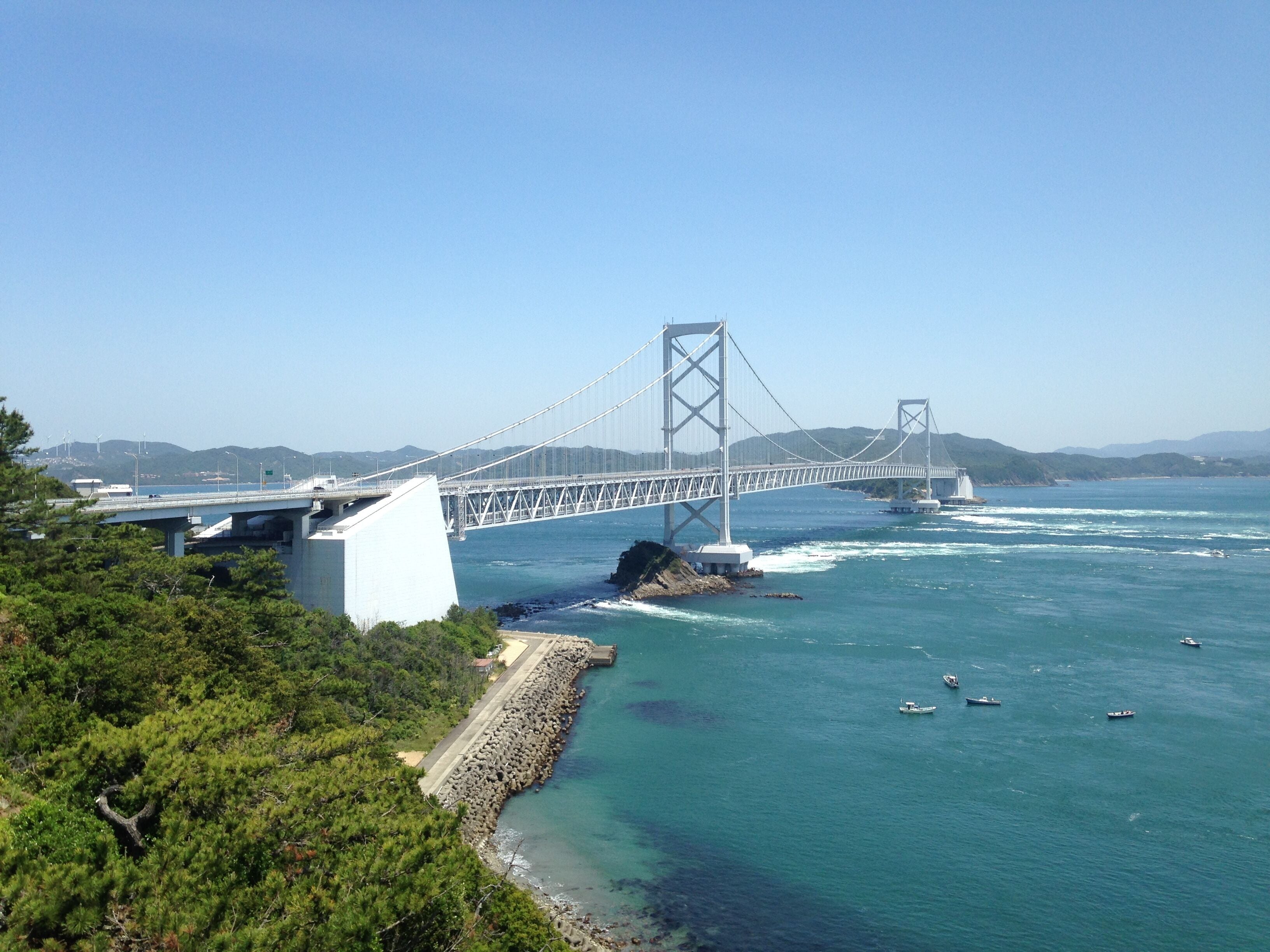 A large suspension bridge spanning a body of water with boats nearby.
