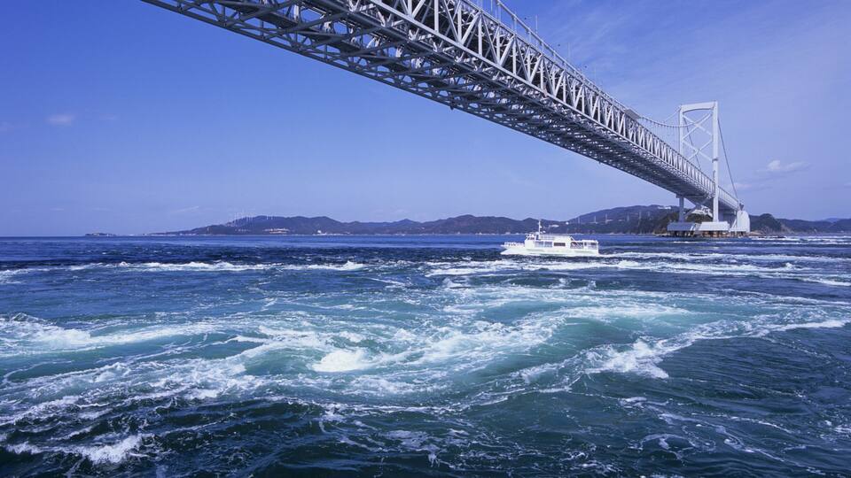 A bridge over turbulent ocean waters with a boat in the foreground.