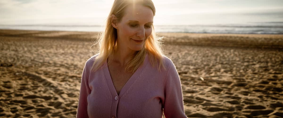 A person standing on a sandy beach with the ocean in the background.