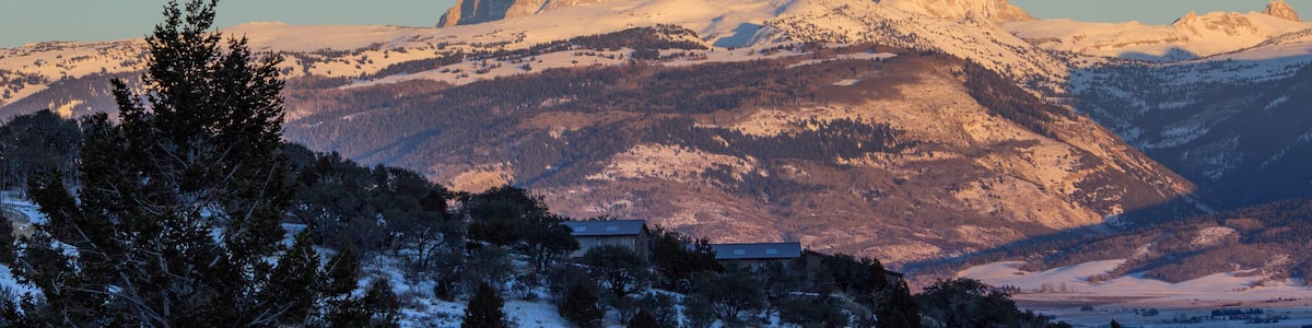 A snow-covered mountain range with a prominent peak, a small building, and a full moon in the sky.