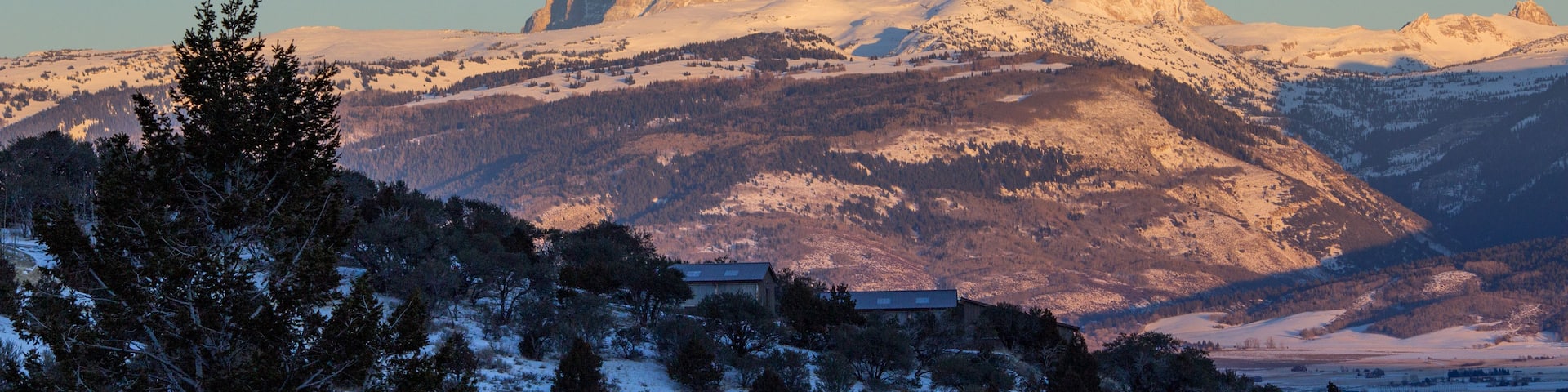A snow-covered mountain range with a prominent peak, a small building, and a full moon in the sky.