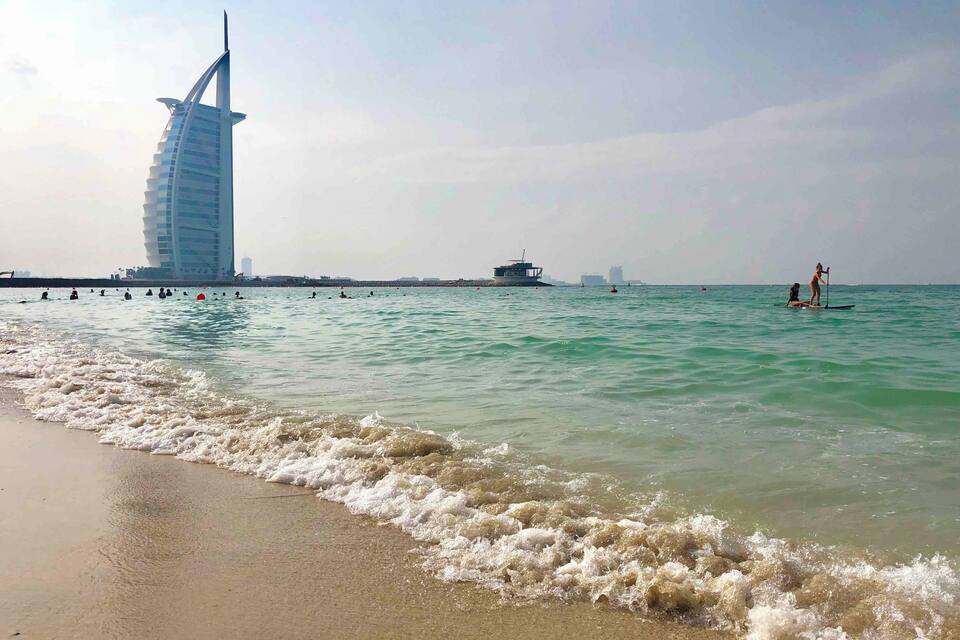 Una playa con olas, un edificio alto y un barco a lo lejos.