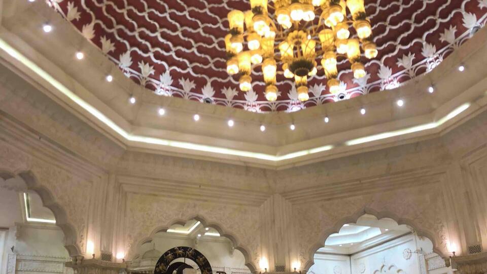 A spacious indoor area with a large, ornate ceiling and a central chandelier. There are seating areas with tables and chairs, and a sign for 'Tutti Frozen' is visible.