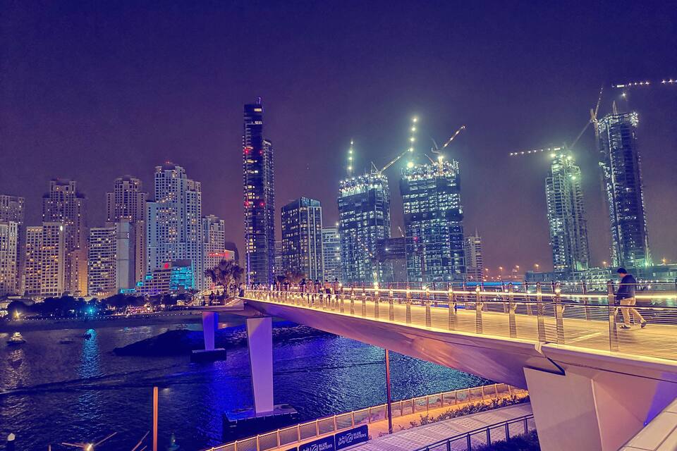 Horizonte urbano noturno com edifícios iluminados e uma ponte sobre o rio.
