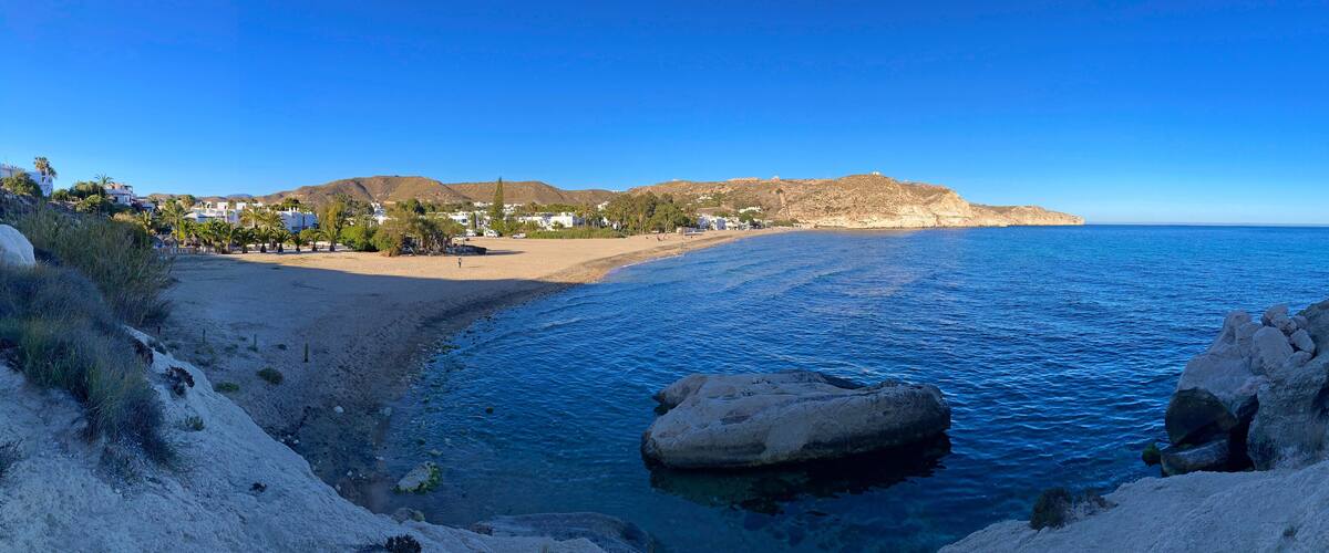 A coastal landscape with a clear blue sea, rocky cliffs, and a sandy beach.