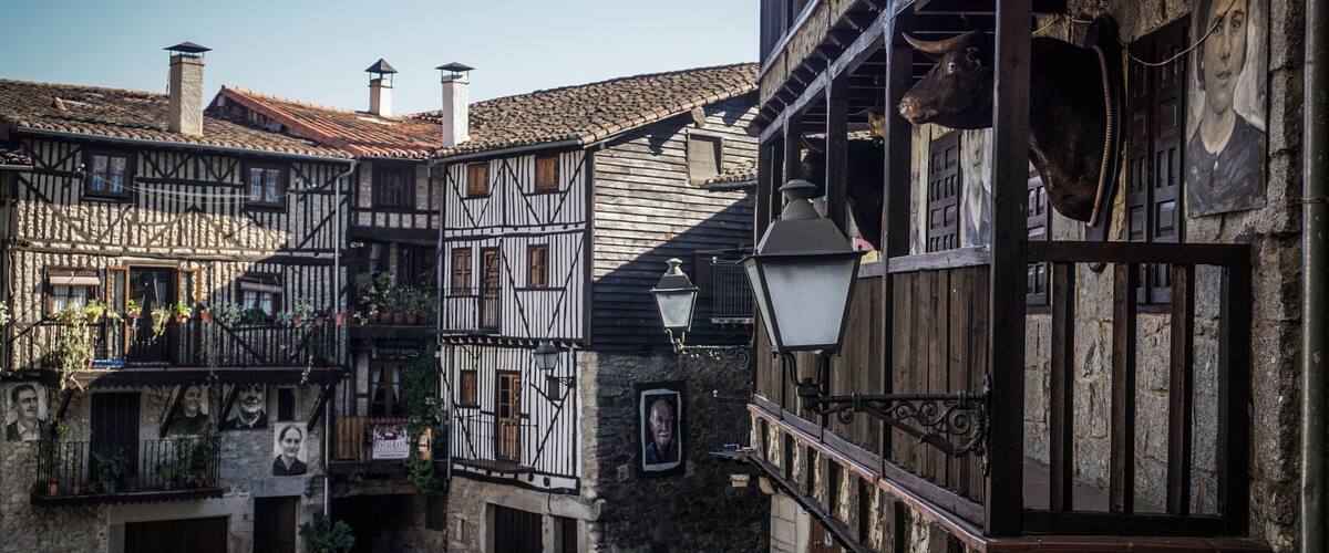 A narrow cobblestone street lined with traditional half-timbered houses, a stone wall, and a hanging lantern.