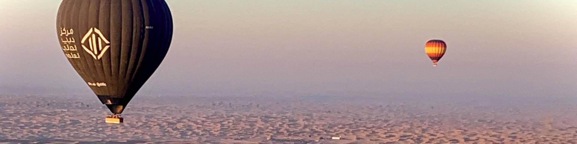 A desert landscape with sand dunes and two hot air balloons.