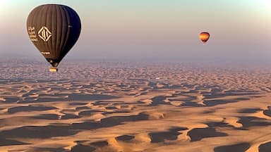 A desert landscape with sand dunes and two hot air balloons.