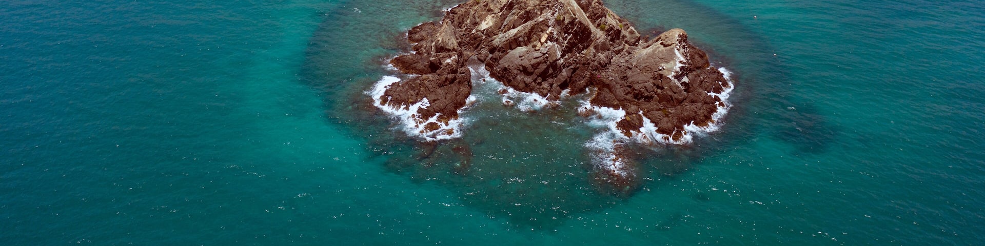 An aerial view of a coastal area with a rocky island, a beach, and a resort complex.