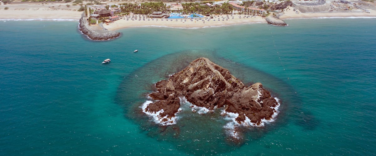 An aerial view of a coastal area with a rocky island, a beach, and a resort complex.