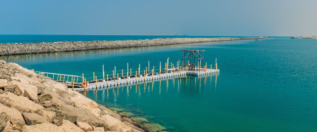 A pier extending into a calm turquoise sea, surrounded by rocky shores and a clear sky.