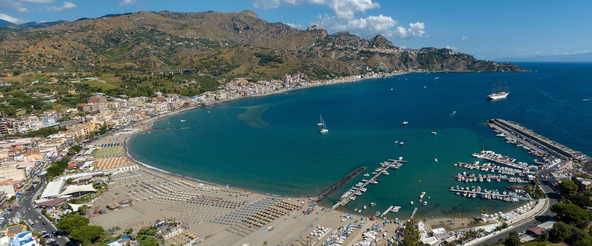 A coastal town with a beach, marina, and mountainous backdrop.