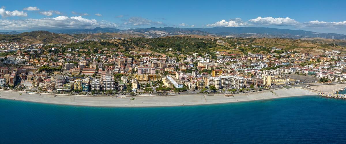 A coastal city with a beach, buildings, and mountains in the background.