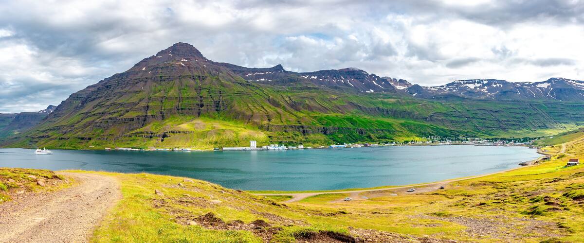 A coastal landscape with a prominent mountain, a body of water, and a small settlement.