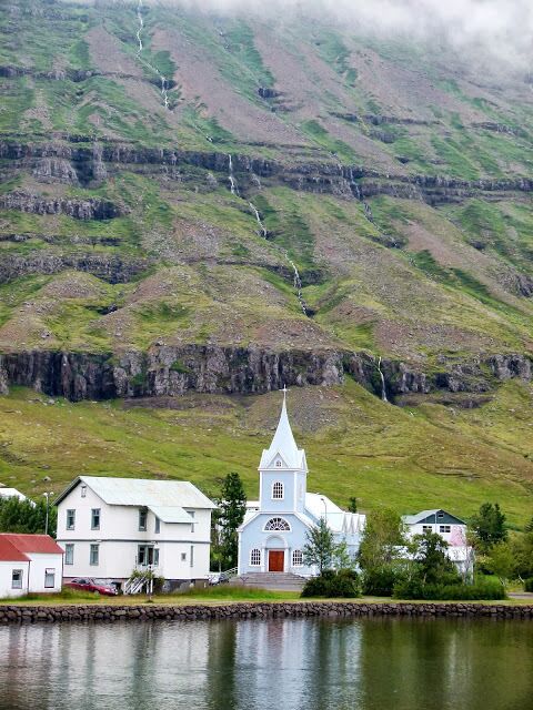 A church with a white steeple, a small white building, and a body of water in front.