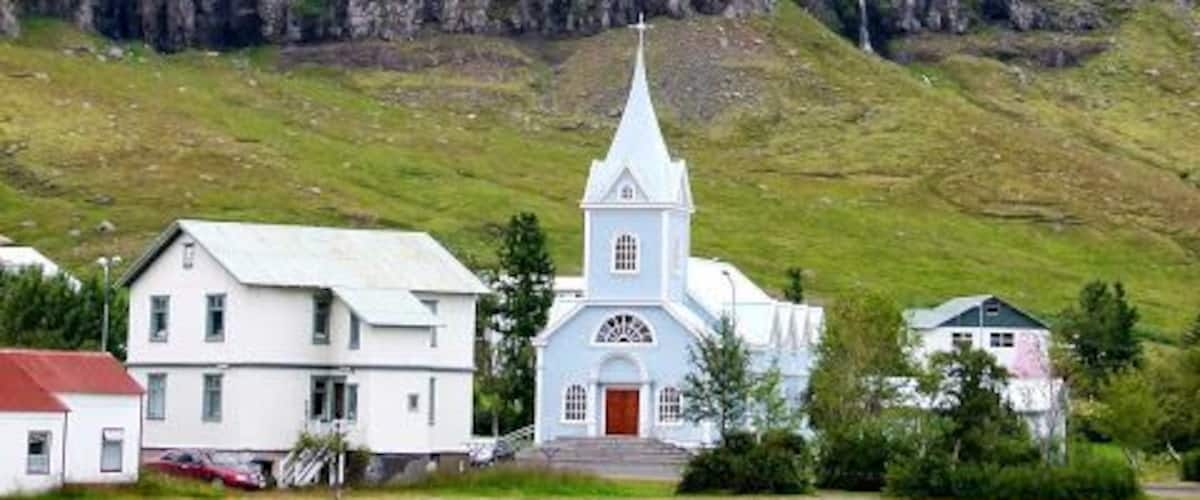 En kyrka med ett vitt torn, en liten vit byggnad och en vattenyta framför.