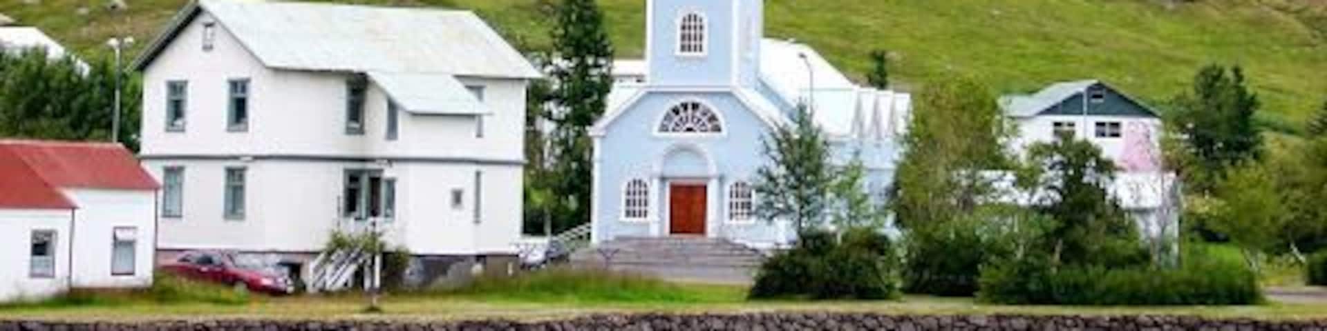 A church with a white steeple, a small white building, and a body of water in front.