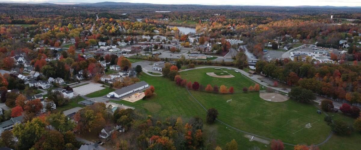 An aerial view of a town with autumn-colored trees, a central green field, and surrounding residential areas.