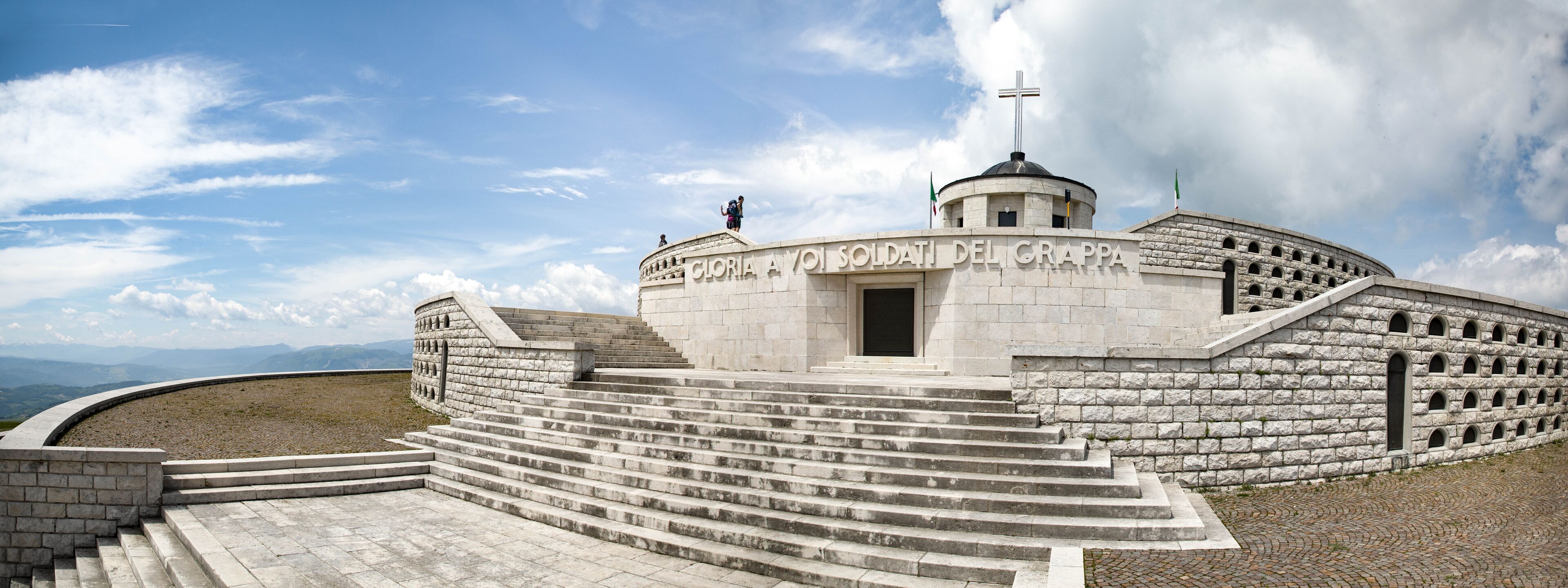 A stone monument with steps leading up to it, a dome, and a cross on top.