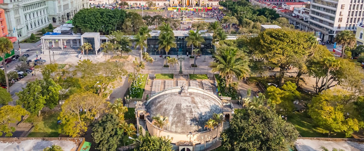 A cityscape with a prominent dome structure surrounded by palm trees and a plaza.