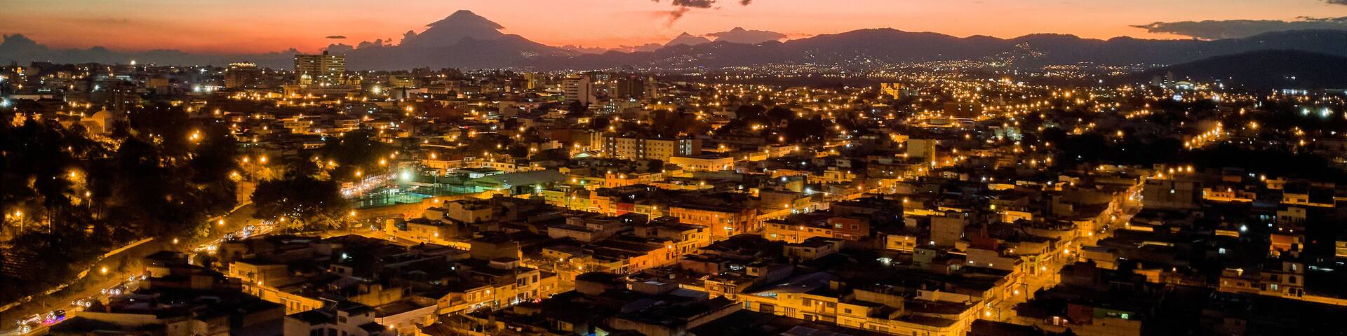 A cityscape at dusk with a mountain in the background.