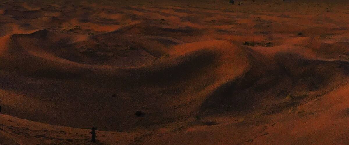 A desert landscape with sand dunes and a sunset sky.