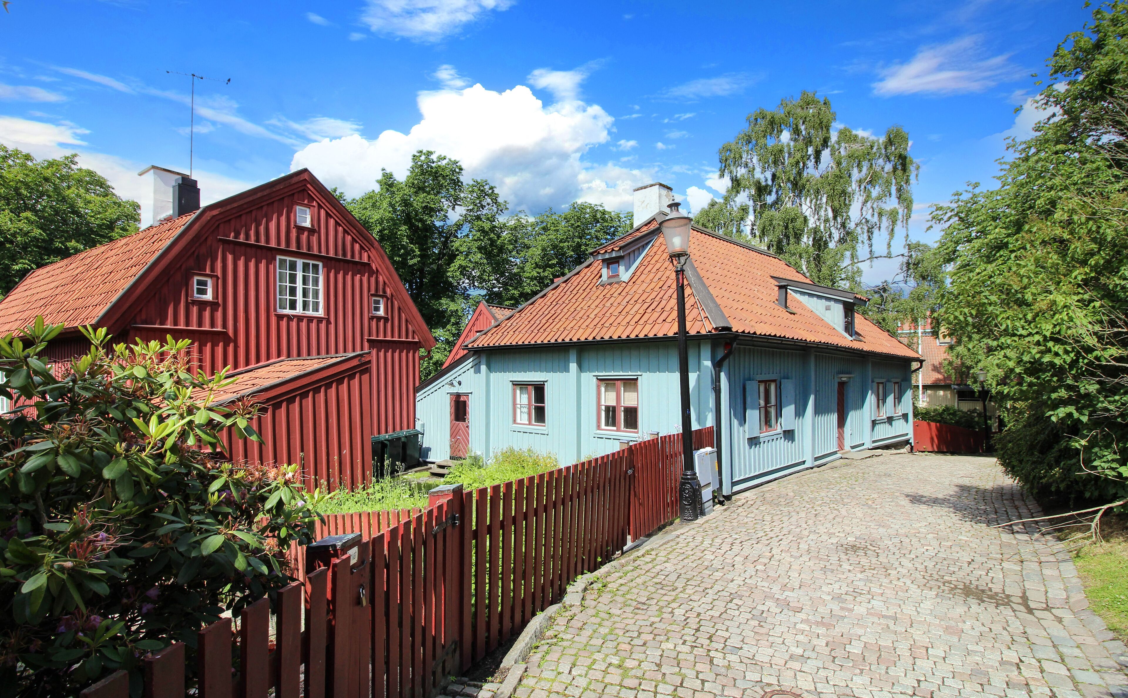 A cobblestone path leading to two traditional houses with red and blue exteriors.