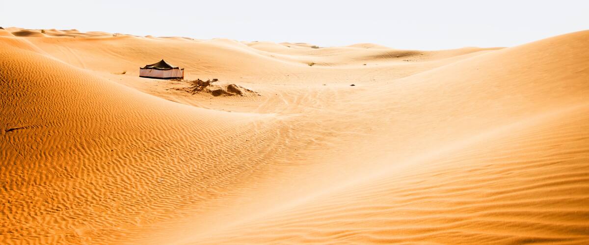 A tent in a desert with sand dunes.