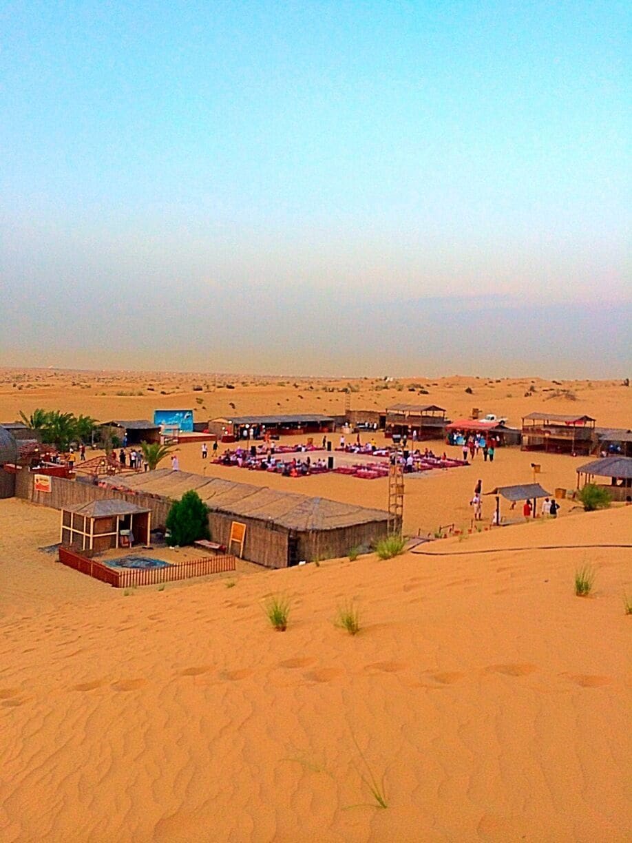 A desert settlement with several small buildings and a large open area with people gathered.