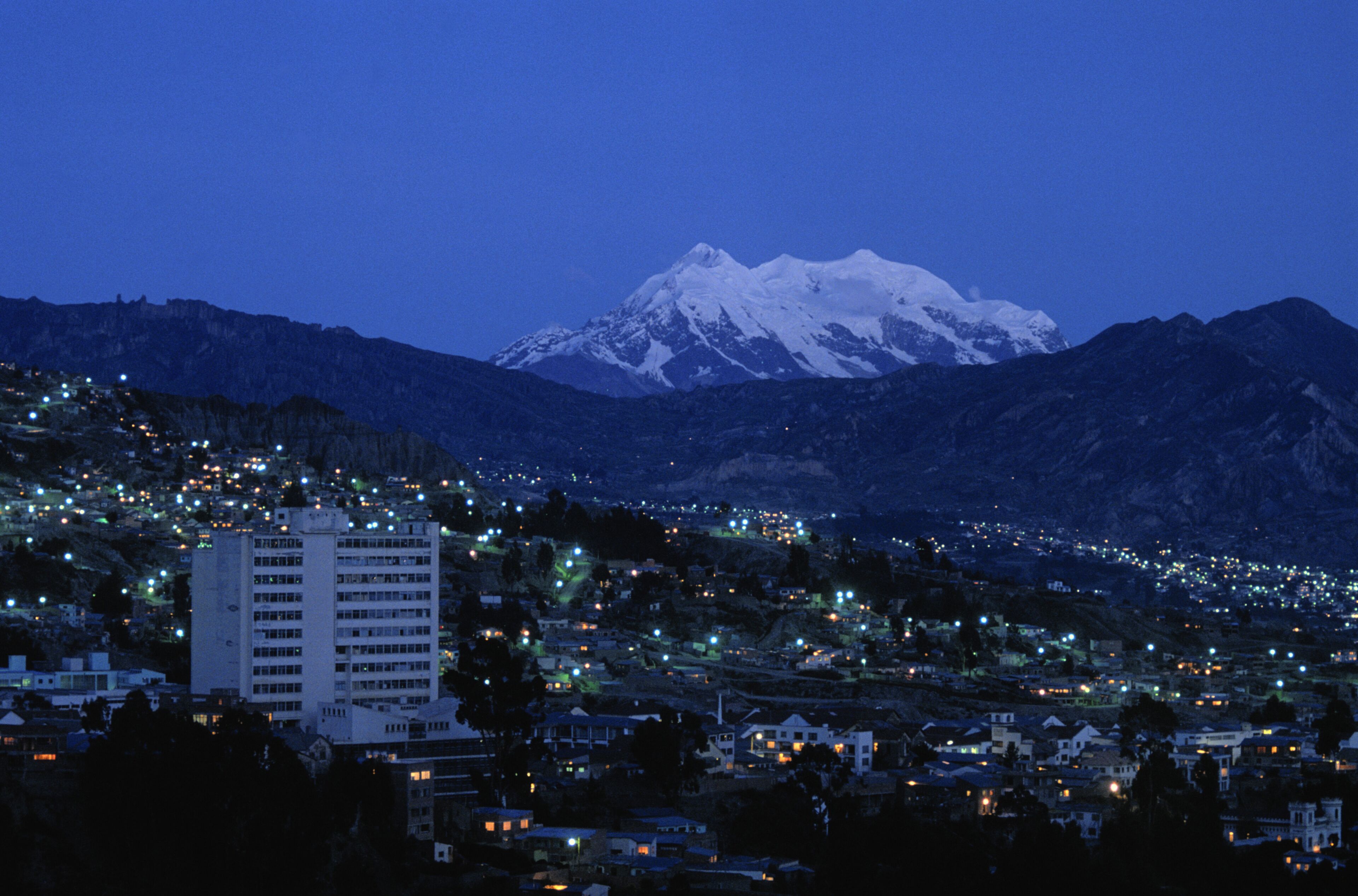 A snow-capped mountain at dusk with a city in the foreground.