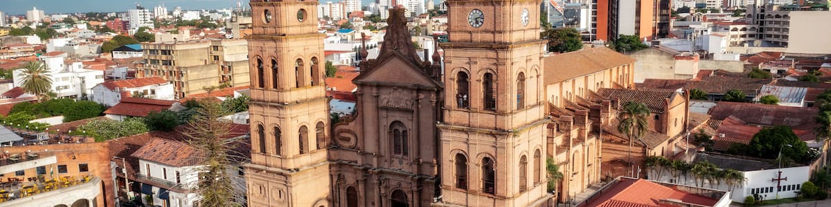 A historic cathedral with two prominent towers, surrounded by urban buildings and palm trees.