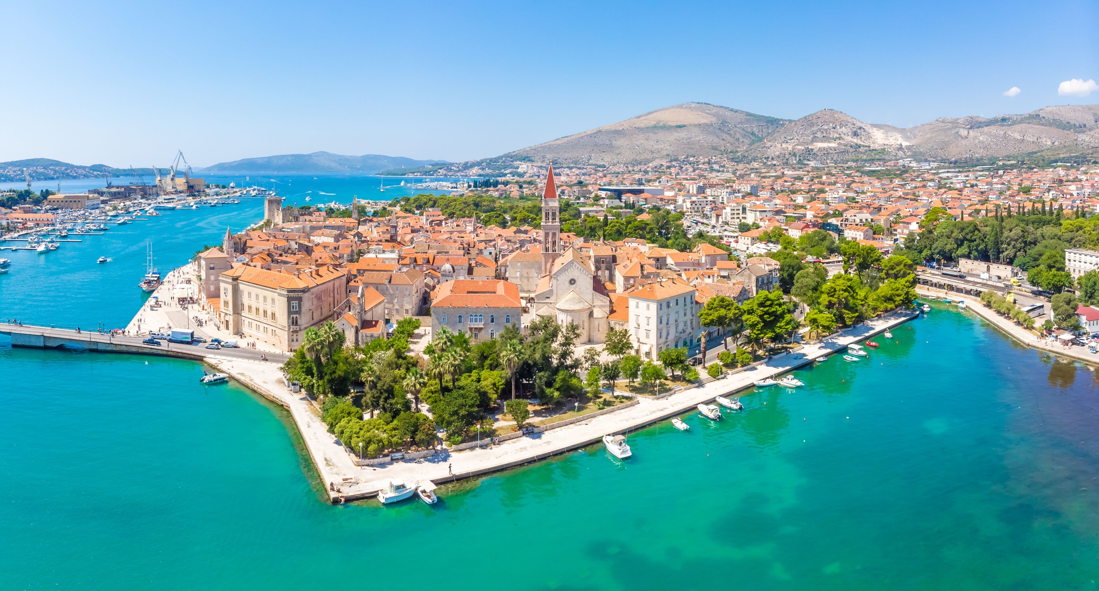 A coastal town with a prominent church, a marina, and a mountainous backdrop.