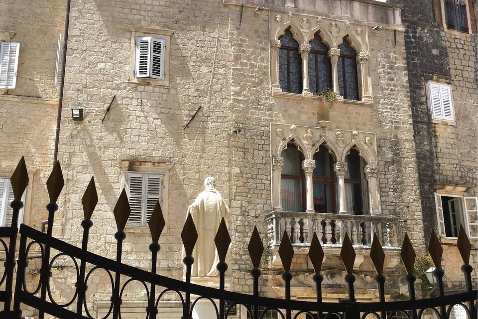A historic stone building with arched windows and a statue in front.