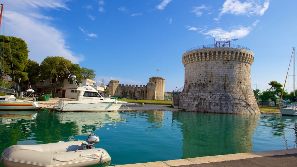 A historic tower by a calm harbor with boats and a castle in the background.